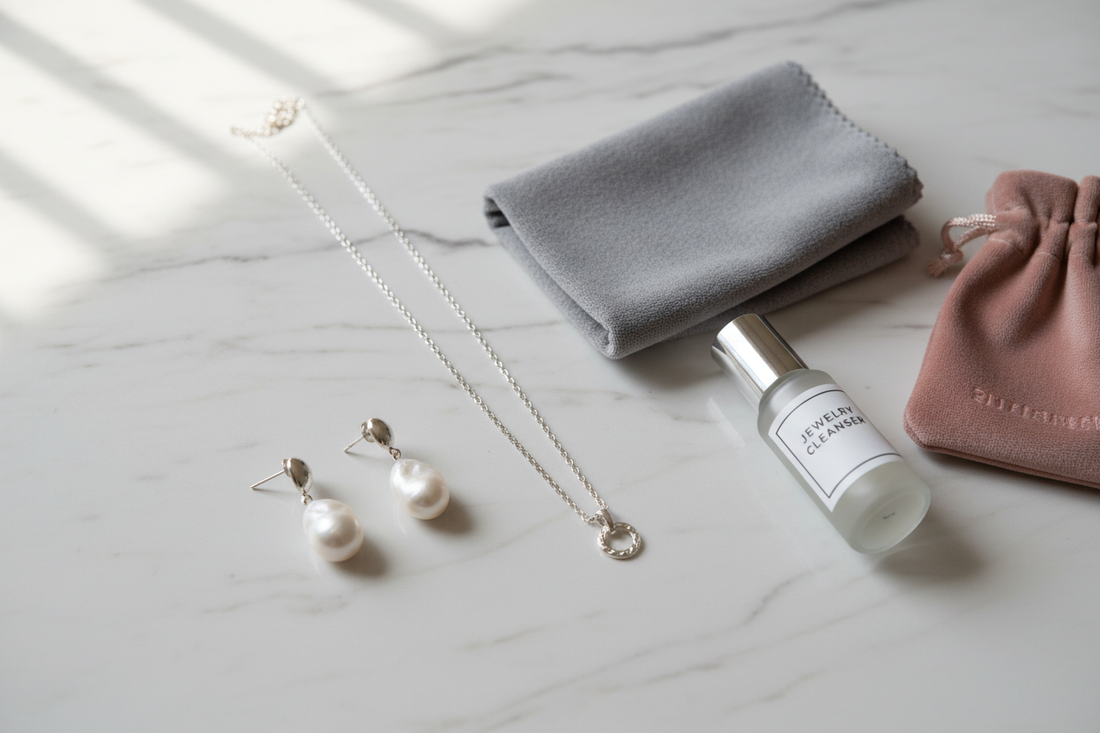925 sterling silver necklace and pearl earrings with jewelry care essentials — polishing cloth, cleaner and velvet pouch on white marble surface