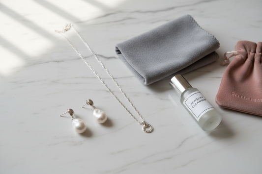 925 sterling silver necklace and pearl earrings with jewelry care essentials — polishing cloth, cleaner and velvet pouch on white marble surface